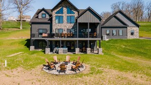 Une maison à deux étages avec une façade en pierre, de grandes fenêtres et une terrasse avec des meubles pour se détendre en plein air.