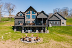 A two-story house with a stone facade, large windows, and a deck with outdoor seating. - The Crooked Oak Lodge - Deep Creek Lake - Indoor Pool & Hot Tub (Deep Creek, Maryland)