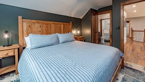Une chambre à coucher avec un grand lit, une tête de lit en bois, des tables de chevet et une petite table de nuit avec une lampe.