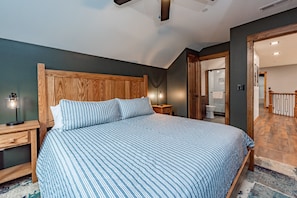 A bedroom with a large bed, wooden headboard, bedside tables, and a nightstand with a lamp. - The Crooked Oak Lodge - Deep Creek Lake - Indoor Pool & Hot Tub (Deep Creek, Maryland)
