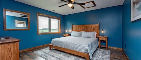 A bedroom with a bed, wooden headboard, nightstands, a desk, a ceiling fan, and a window with a view.