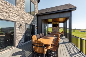 A deck with a long wooden table and chairs, a stone wall, and a view of the countryside. - The Crooked Oak Lodge - Deep Creek Lake - Indoor Pool & Hot Tub (Deep Creek, Maryland)