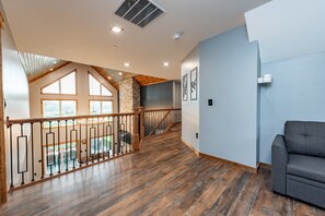 A spacious interior with a wooden staircase, a balcony with a view, and a grey sofa.