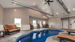 Une piscine dont les bords sont recouverts de carreaux, avec des bancs en bois et des chaises disposés tout autour.