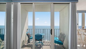 Un balcon avec vue sur l’océan, doté d’une porte-fenêtre coulissante, de deux chaises bleues et d’une table.