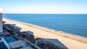Vue sur la plage depuis un immeuble de grande hauteur, avec un court de tennis et une piscine au premier plan.