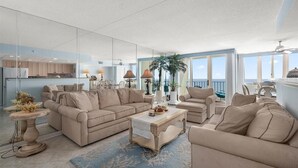 Un vaste salon comprenant un grand canapé, une table basse et un coin repas avec des chaises. Il y a également un balcon avec vue sur l’océan.