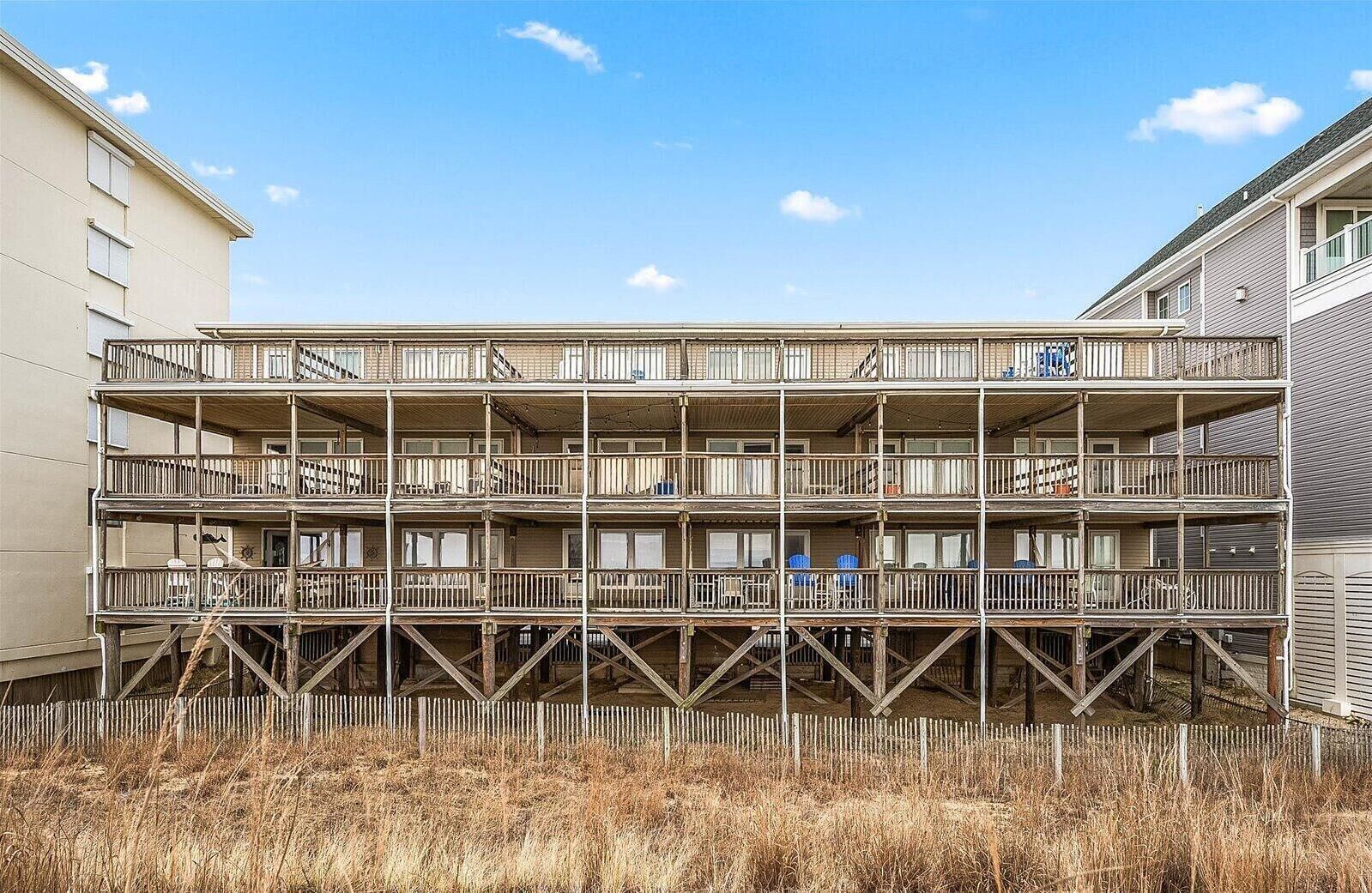 A multi-story building with balconies, wooden railings, and a fenced area in front.