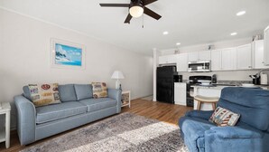 A modern living room with a sofa, a blue armchair, a patterned rug, and a ceiling fan. - Windbreaker - Amazing Views From This 1 Bedroom Oceanfront Condo (Ocean City)