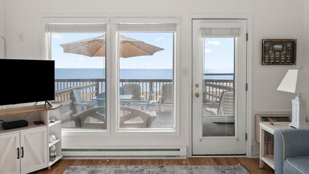 A room with a television, a desk, and a view of the ocean through a glass door. - Windbreaker - Amazing Views From This 1 Bedroom Oceanfront Condo (Ocean City)