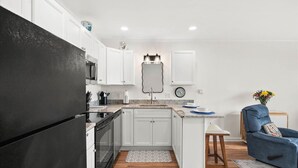 A modern kitchen with white cabinets, a black refrigerator, and a wooden floor. - Windbreaker - Amazing Views From This 1 Bedroom Oceanfront Condo (Ocean City)