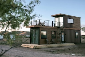 A modern, multi-level cabin with a balcony, large windows, and a staircase.
