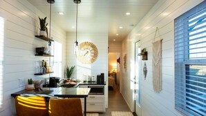 A modern kitchen with a central island, pendant lights, and a large wall clock. - Somewhere in Texas Container Home (Alpine)