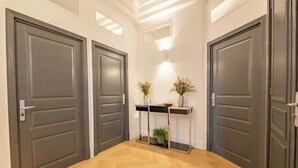 Un couloir avec deux portes sombres, une petite console sur laquelle sont posés un vase et une plante, et un luminaire au plafond.