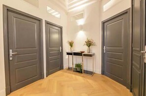 Ein Flur mit zwei dunklen Türen, einem kleinen Konsolentisch mit Vase und Pflanze sowie einer Leuchte darüber.