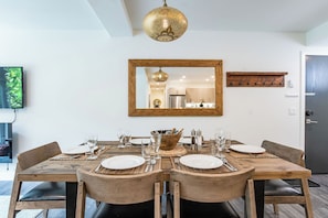 A dining area with a wooden table set for six, a large mirror above, and a hanging gold pendant light.