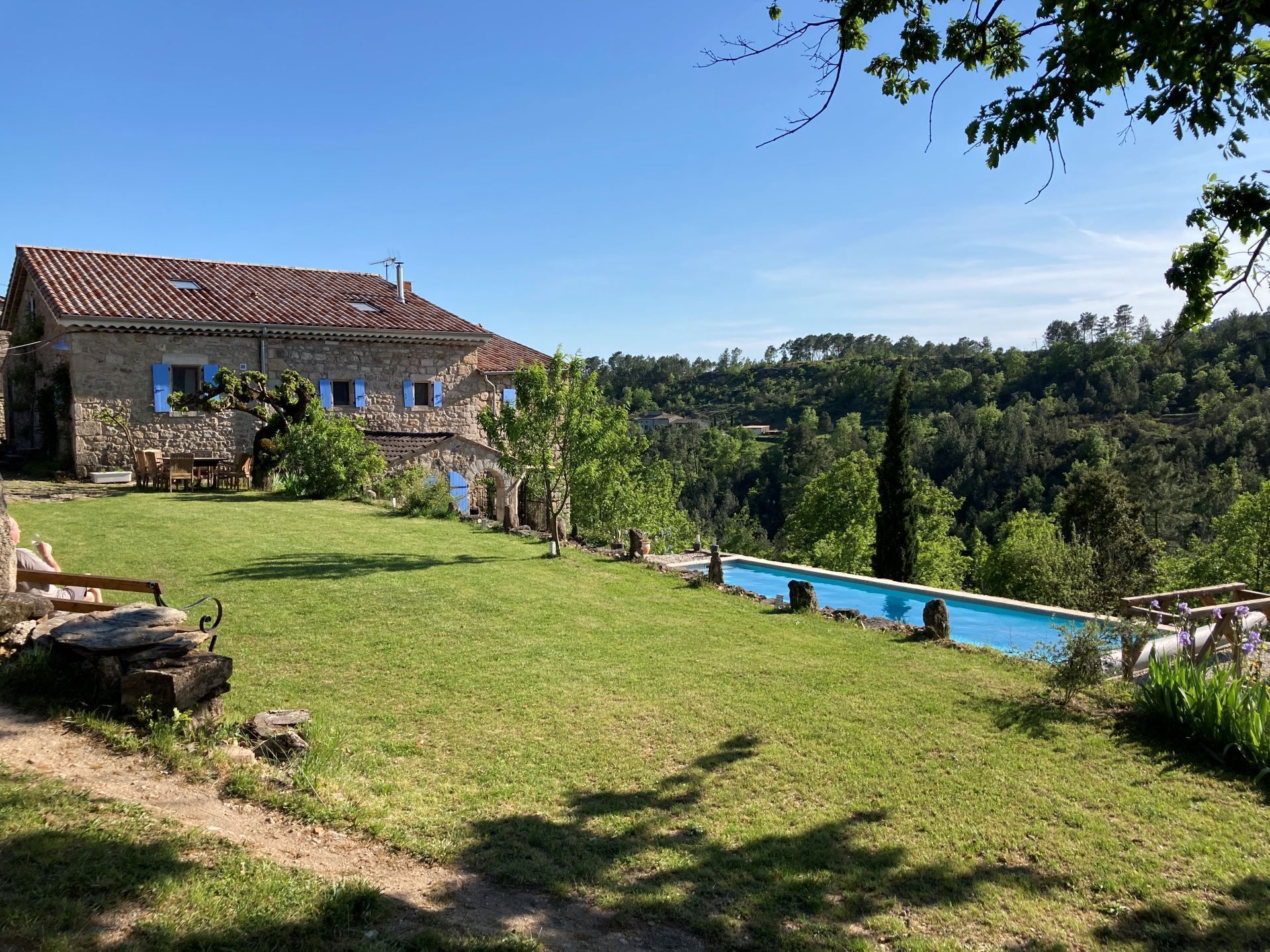 A stone house with a swimming pool, surrounded by a lush green lawn and trees.
