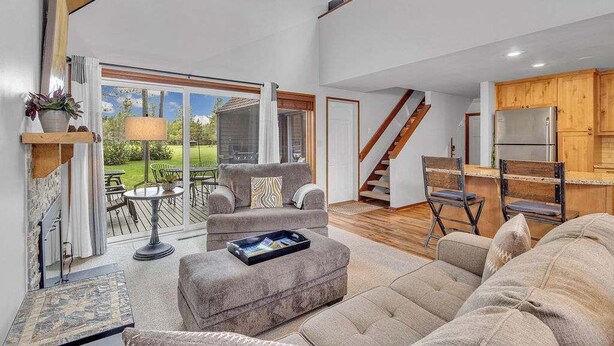 A spacious living area with a sofa, ottoman, and a dining table. A kitchen with wooden cabinets and a refrigerator is visible in the background. - Updated, great location, by Sharc and Village mall (Sunriver)