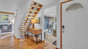 A modern interior with a wooden staircase, a white door with a decorative glass panel, and a cozy seating area with a fireplace. - Updated, great location, by Sharc and Village mall (Sunriver)