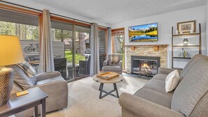 A living room with a fireplace, a sofa, a coffee table, and a TV. - Updated, great location, by Sharc and Village mall (Sunriver)