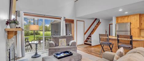 A spacious living area with a sofa, a coffee table, and a dining table. There is a staircase leading to an upper level.