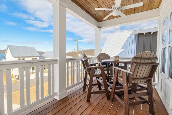 A covered outdoor area with a wooden deck, a table, two chairs, and a ceiling fan.