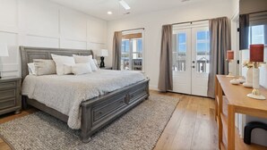 A bedroom with a large bed, a ceiling fan, a nightstand, a dresser, a wooden table with candles, and a view through a glass door.