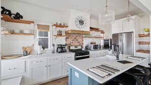 A modern kitchen with white cabinetry, a central island, a brick backsplash, and stainless steel appliances.