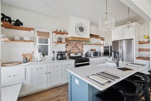 A modern kitchen with white cabinetry, a central island, a brick backsplash, and stainless steel appliances.