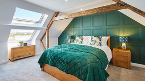 Une chambre avec un plafond en pente, un grand lit recouvert d’une couette verte, des tables de chevet en bois et un puits de lumière.