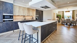 Une cuisine moderne dotée d’un grand îlot central, de tabourets de bar et d’un coin repas agrémenté d’un lustre.