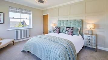 A bedroom with a large bed, a window with blinds, a radiator, a door, and a nightstand with a lamp.