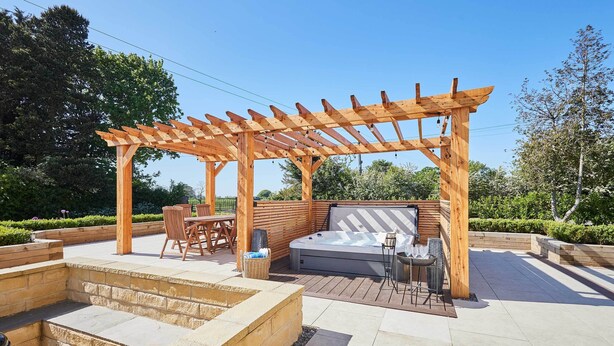 Une structure de pergola en bois avec un jacuzzi et un espace salon.