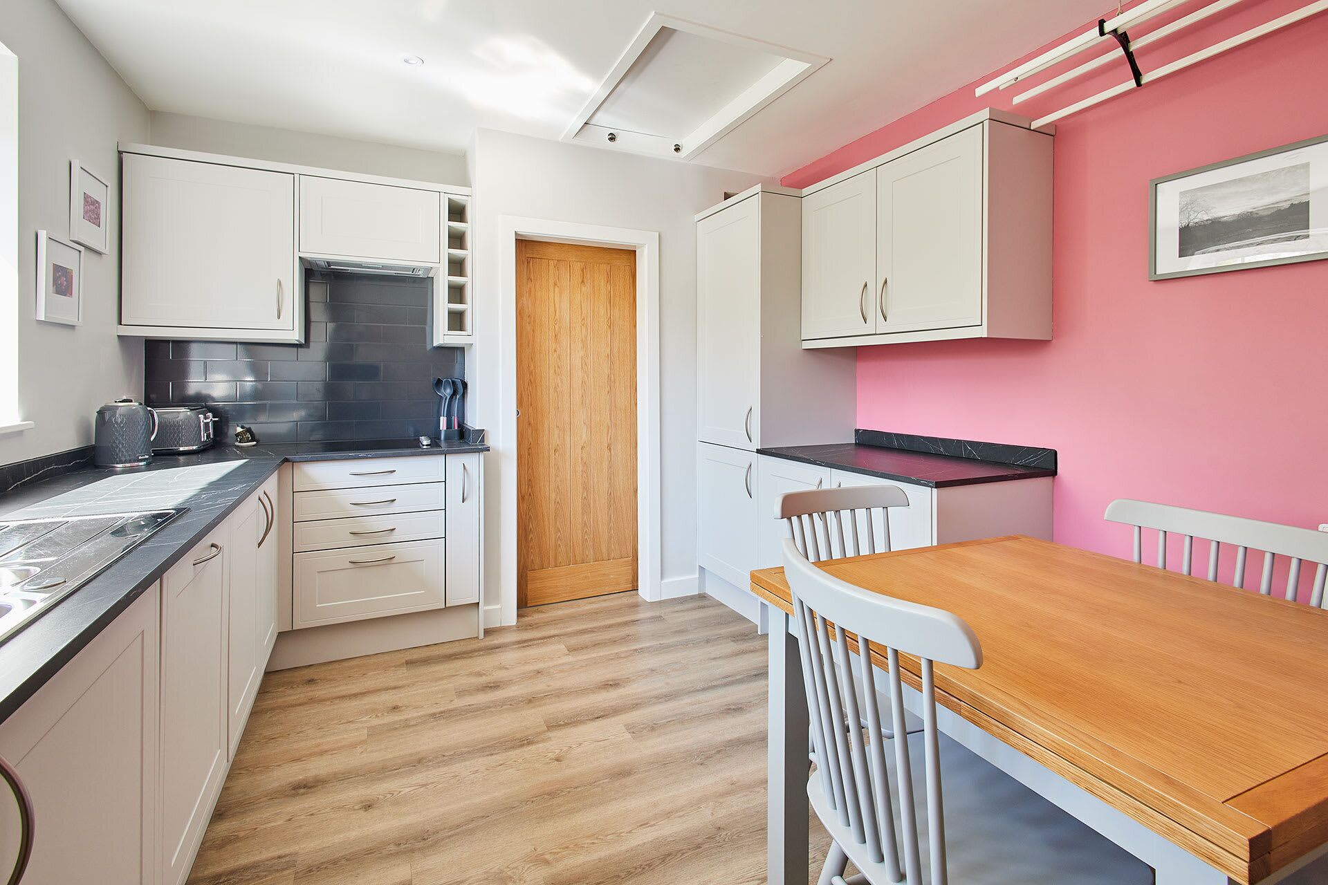 A compact kitchen with white cabinets, a wooden door, and a dining area with a wooden table and white chairs.