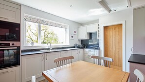 Une cuisine moderne avec des meubles blancs, une table à manger en bois et une fenêtre donnant sur les arbres.