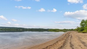 Una playa arenosa con un lago tranquilo y colinas a lo lejos.