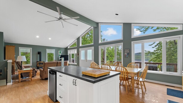 Una cocina amplia con una isla central, mesa de comedor de madera y sillas, ventanas grandes y un ventilador de techo.