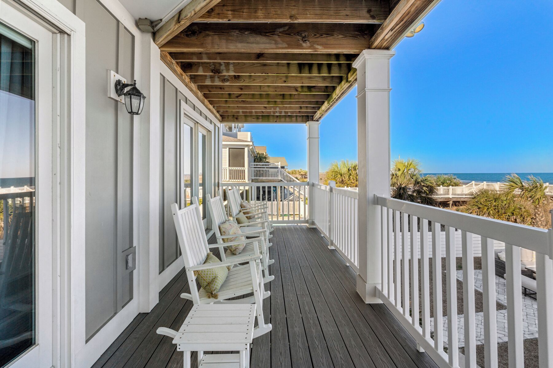 A wooden deck with white railings and chairs, overlooking a beach and ocean.