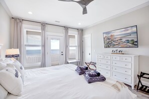 Une chambre d’hôtel avec un lit, une commode blanche, un tableau représentant une ville côtière et une vue sur la mer par la fenêtre.