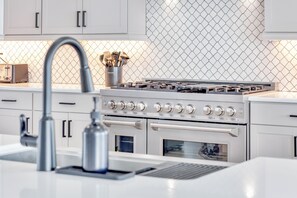 A modern kitchen with white cabinets, a stainless steel range, and a backsplash with a diamond pattern. - Serenity Hideaway: Oceanfront w/ Pool & Stunning Views (North Myrtle Beach)