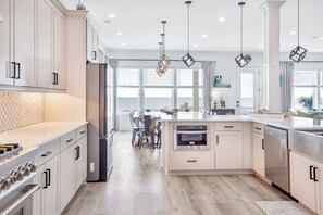 Une cuisine moderne avec des meubles blancs, un îlot central, des appareils en acier inoxydable et des luminaires suspendus.
