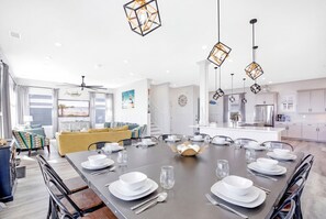 A modern dining area with a large table set for six, surrounded by a living room with a sofa and a view of the kitchen. - Serenity Hideaway: Oceanfront w/ Pool & Stunning Views (North Myrtle Beach)