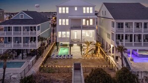 A two-story house with a pool, deck chairs, and a staircase leading to a balcony.
