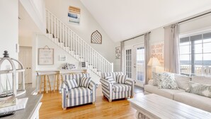 A spacious living room with a staircase, striped armchairs, a sofa, and a view of the sea.