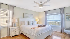 A bedroom with a bed, bedside tables, a ceiling fan, and a view of the ocean.