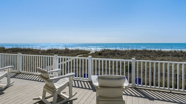 A wooden deck with white railings overlooking a beach.