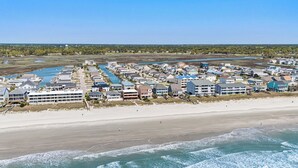 Eine Luftaufnahme einer Küstenwohngegend mit Strandhäusern, einem Jachthafen und einem Leuchtturm in der Ferne.