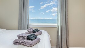 Ein Hotelzimmer mit Bett, einem Fenster mit Meerblick und Handtüchern mit einem Logo.