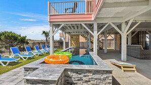 Ein Außenpoolbereich mit Liegestühlen, einer Holzterrasse und einem überdachten Sitzbereich.