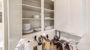 Una cocina con armarios abiertos que muestran platos y tazones apilados, una cafetera y una licuadora sobre la encimera.